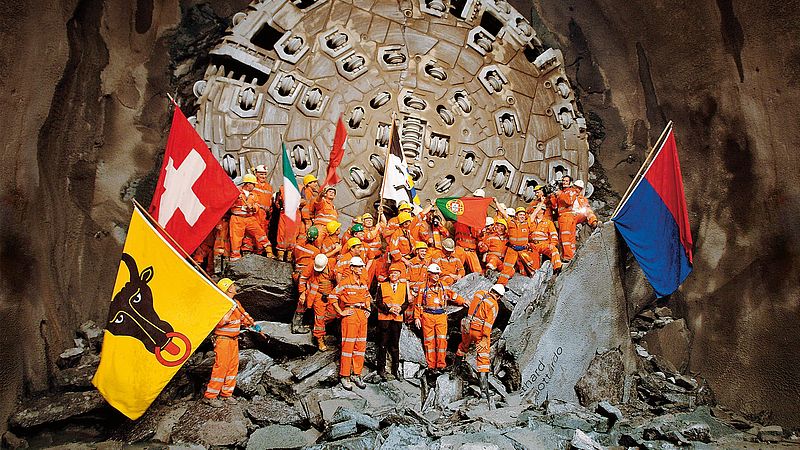 高塔基地隧道最终贯通后，施工现场人员站在隧道掘进机前挥舞旗帜。